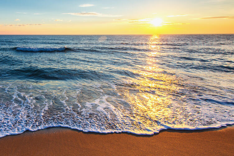 a ripple of ocean Blonde-haired woman relaxes on a cliff, looking out at the Pacific Ocean on a beautiful day. She is wearing a light colored t-shirt with an army green cardigan and light jeans.