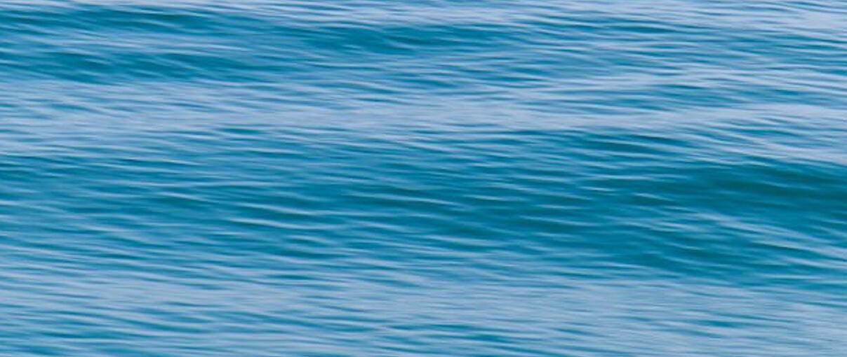 MIchelle, recharging, in Santa Cruz, CA Blonde-haired woman relaxes on a cliff, looking out at the Pacific Ocean on a beautiful day. She is wearing a light colored t-shirt with an army green cardigan and light jeans.
