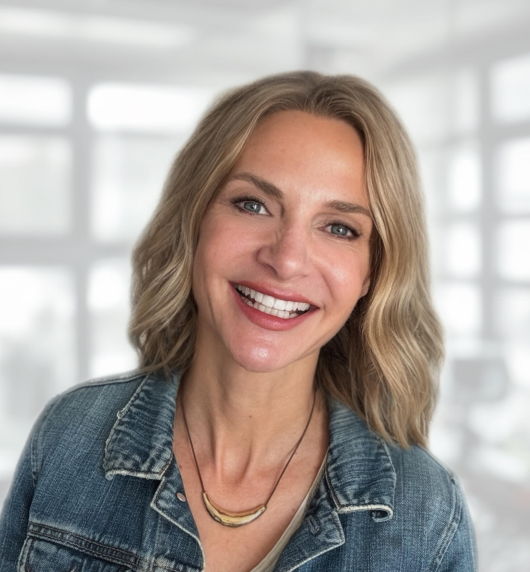 MIchelle Waters, Founder of Waters Edge Co Close-up headshot of blonde-haired woman smiling for the camera. She is wearing a light colored denim jacket.